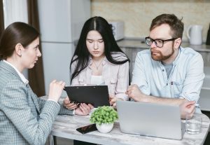 Couple sitting as a desk with paperwork and a computer talking with a bank manager about opening multiple joint accounts