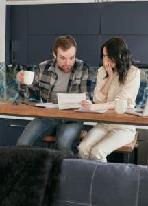 A couple sitting at a bench looking over some paper work and the man seems very suprised.