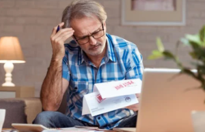 A man sitting in front of bills, looking upset and thinking about bankruptcy